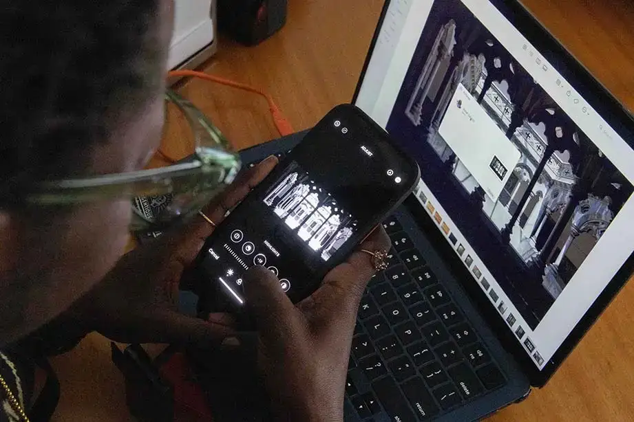 A student uses their phone and laptop to edit digital black and white photos.
