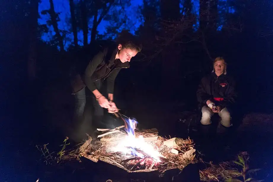 Student tends to a campfire at night at the College Camp.