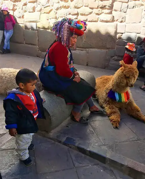 Photo by Rebecca Price of a colorfully-dressed indigenous woman and her child sitting with a llama in Cusco, Peru.