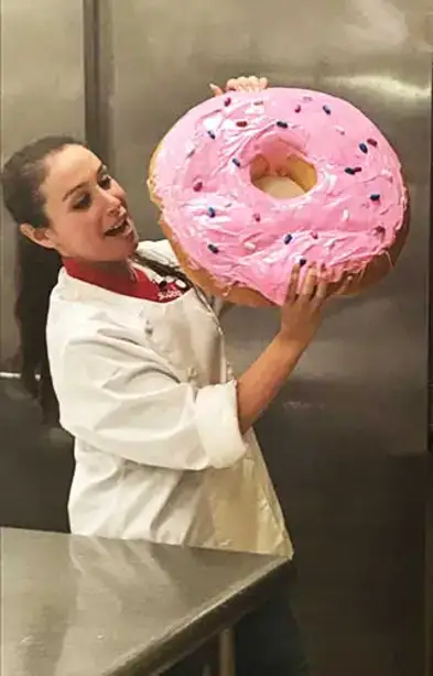 Julia Goolia pretends to eat a giant donut frosted with pink frosting.
