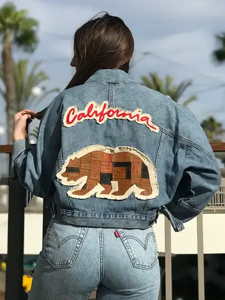 Model wears a denim jacket featuring the word California along with a patchwork silhouette of a bear.