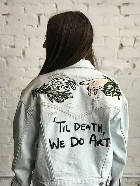 Model wears a denim jacket with the words 'Til Death, We Do Art.