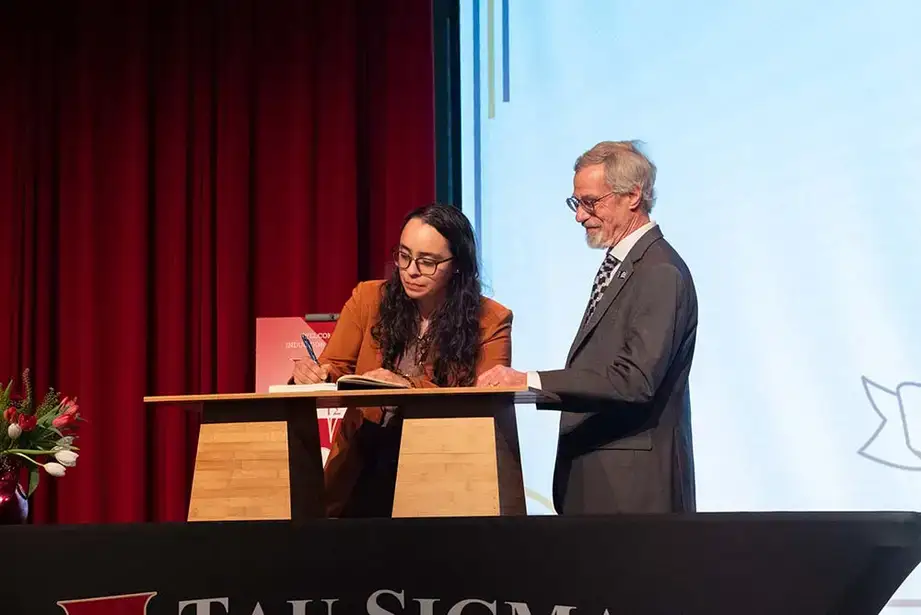 Co-Advisor Ron Bishop watches as student inductee Diana Chavez sings the membership book.