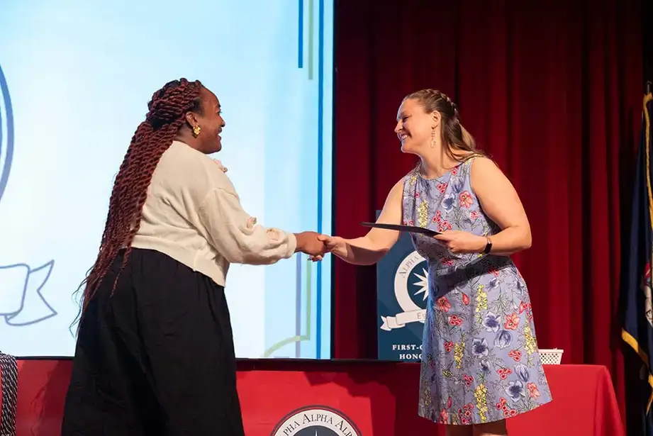 A student inductee receives her membership certificate from Co-Advisor Sarah Wells.