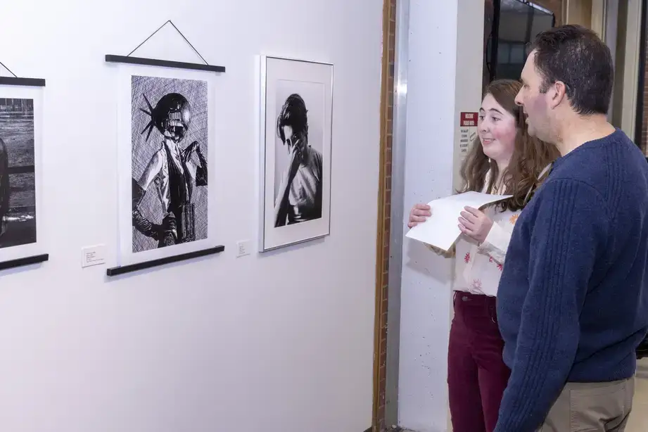 An exhibitor and visitor discuss an exhibit of fine art during a Juried Student Show