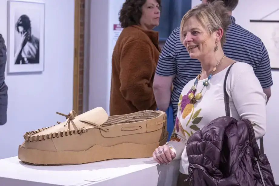 Visitors to a Juried Student Show stand near a particularly large cardboard moccasin shoe sculpture exhibit.