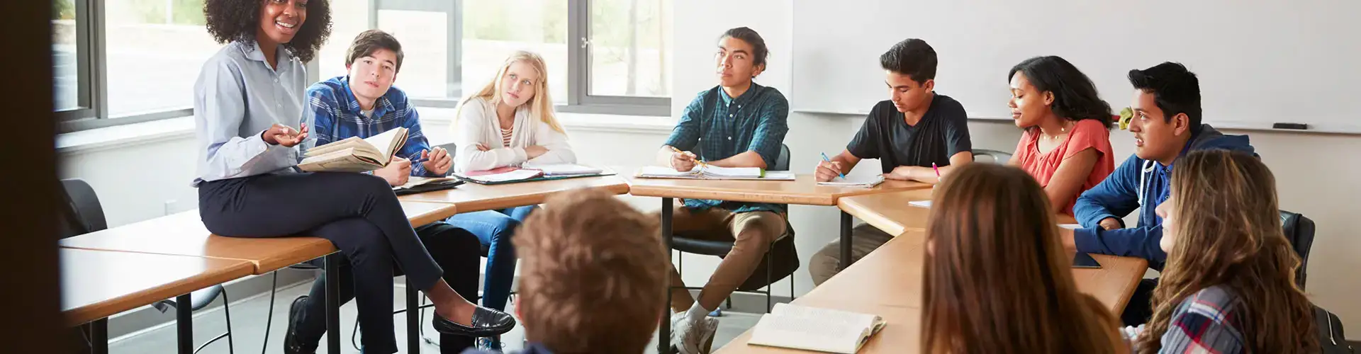 Female High School Spanish Teacher Sitting At Table With Pupils
