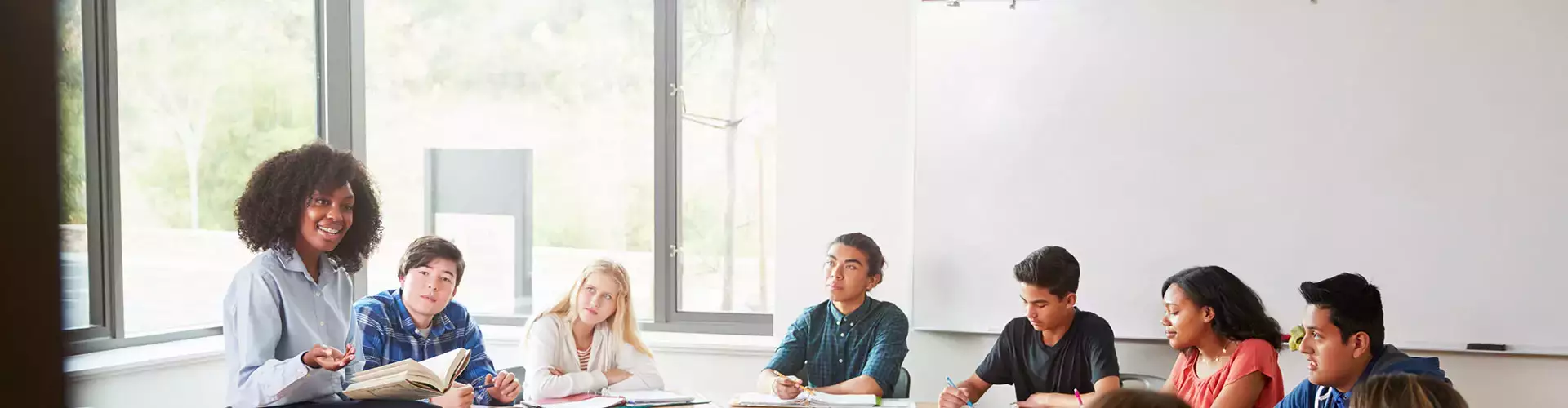Female High School Spanish Teacher Sitting At Table With Pupils