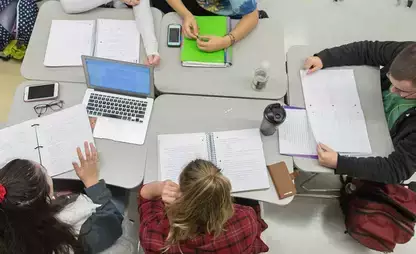 view from above of people working at a workspace covered in notebooks, binders and a laptop