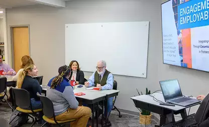 modern workspace with people sitting at tables and a presenter working at a laptop and large display