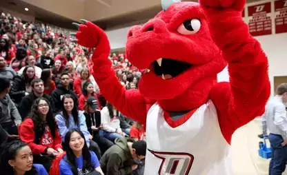 SUNY Oneonta's mascot, Red, in front of bleachers full of fans at a basketball game