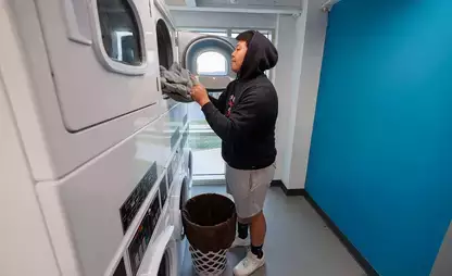 Student removing their laundry from a dryer in their residence hall's laundry room