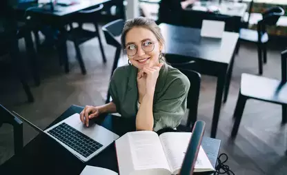 Smiling person sitting at laptop and looking at camera while studying