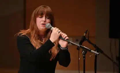 Student singer with their eyes closed and hands on a microphone during a musical performance