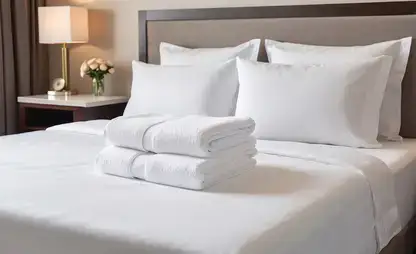 Nicely made bed with white linens with towels folded on top, with a bedside table