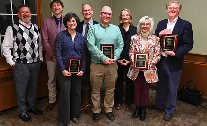 Posed photo: Community of Scholars award winners holding awards, deans and the provost