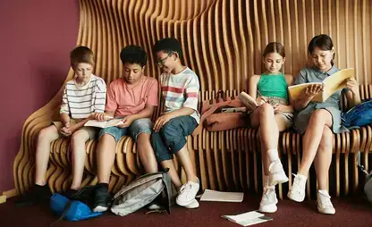 Elementary students sit on a sculptural bench and read.