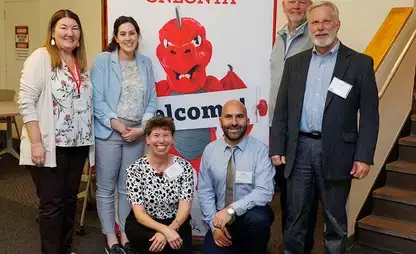 EAS Advisory Council poses in front of a SUNY Oneonta Red Dragons sign.