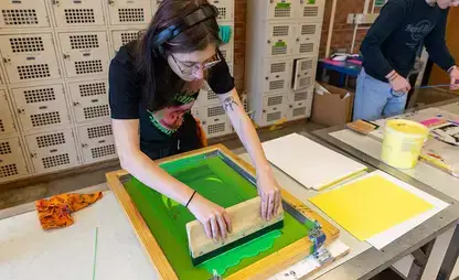Student draws a squeegee across a screen print.