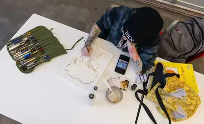 Overhead view of a student sketching in a notebook while seated at a desk.