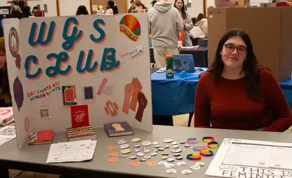 Student sits at a table with a poster board describing the WGS Club.