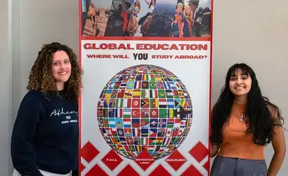 Students pose next to a large poster board sign promoting global education and study abroad.