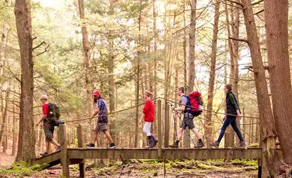 Students cross a bridge in the forest at College Camp.