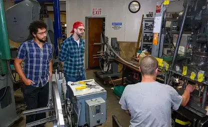 Participants n the manufacturing workshop watch a machine demonstration.