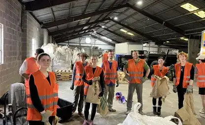 Group of students wearing orange safety vests pose in a large warehouse.