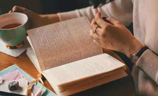 An individual reads through their journal while enjoying a cup of coffee