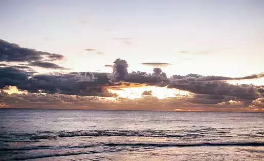 The sun illuminates a series of clouds far off over the ocean