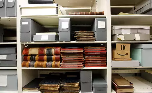 Stacks of old hard bound books sit on a shelf of the archives