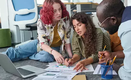 Two young women pointing at a document of charts during statistics discussion