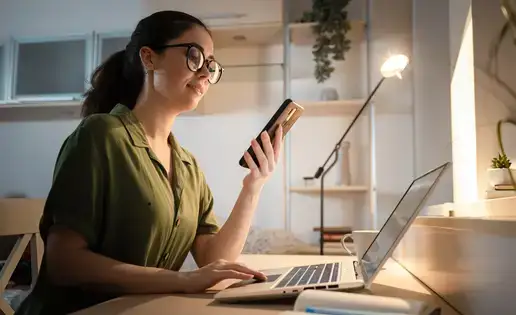 Caucasian smiling young person using cellphone and working at laptop.