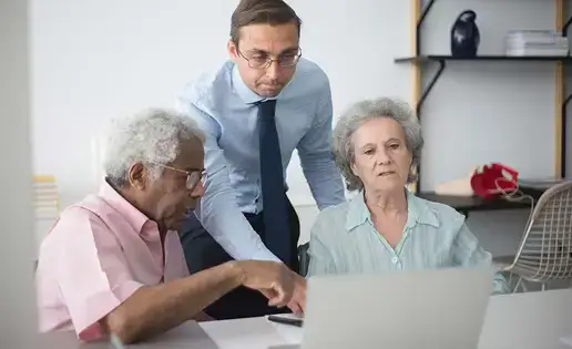 A man in a shirt and tie helps a diverse elderly couple with a computer.