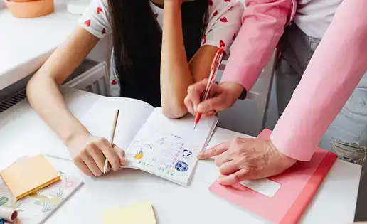 A teacher helps a student with a notebook exercise.