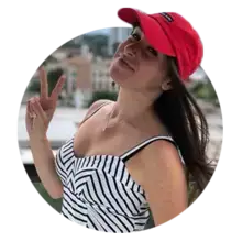Julia Goolia wearing a red baseball cap holding up two fingers suggesting the peace sign.