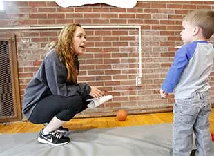 Female student crouching to talk to a little boy.
