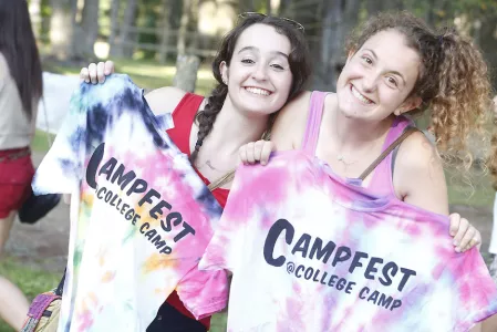 Two girls holding up tye-die shirts that say Campfest on them.