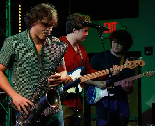 Music students playing the saxophone, guitar, and bass guitar.