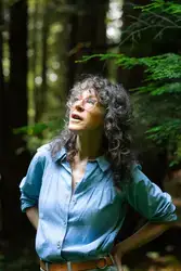 Author Jennifer Kabat poses among the trees of a forest.