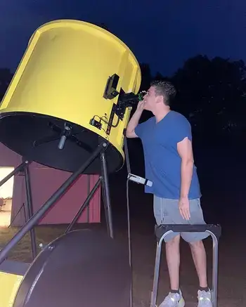 Student looks into a large telescope at night.